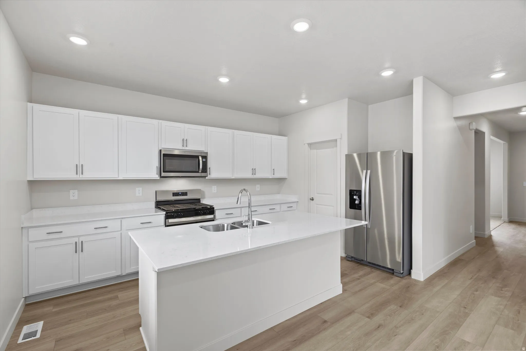 Kitchen featuring stainless steel appliances, light wood-type flooring, white cabinets, a center island with sink, and recessed lighting