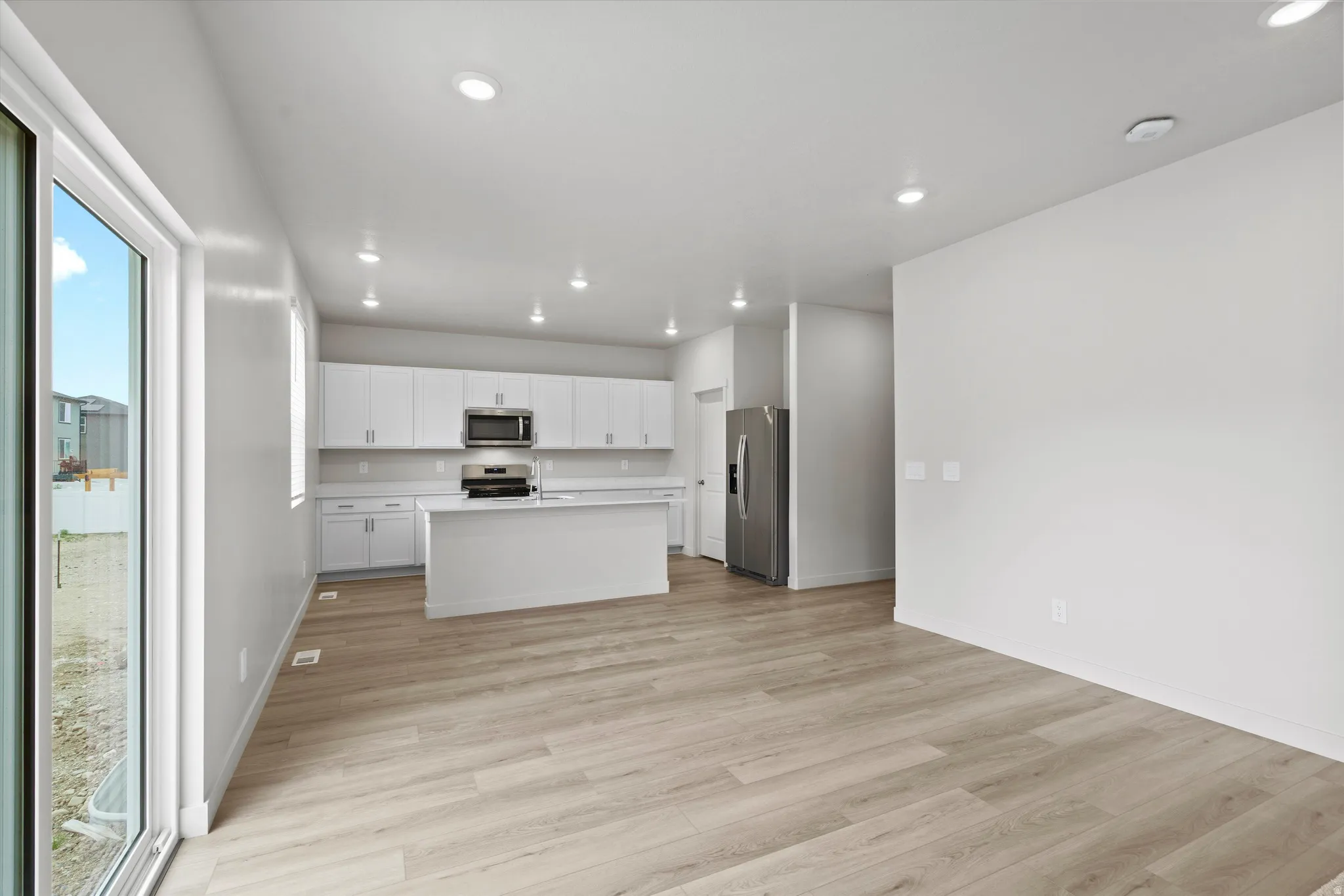 Kitchen with light countertops, white cabinetry, a kitchen island with sink, light wood finished floors, and recessed lighting