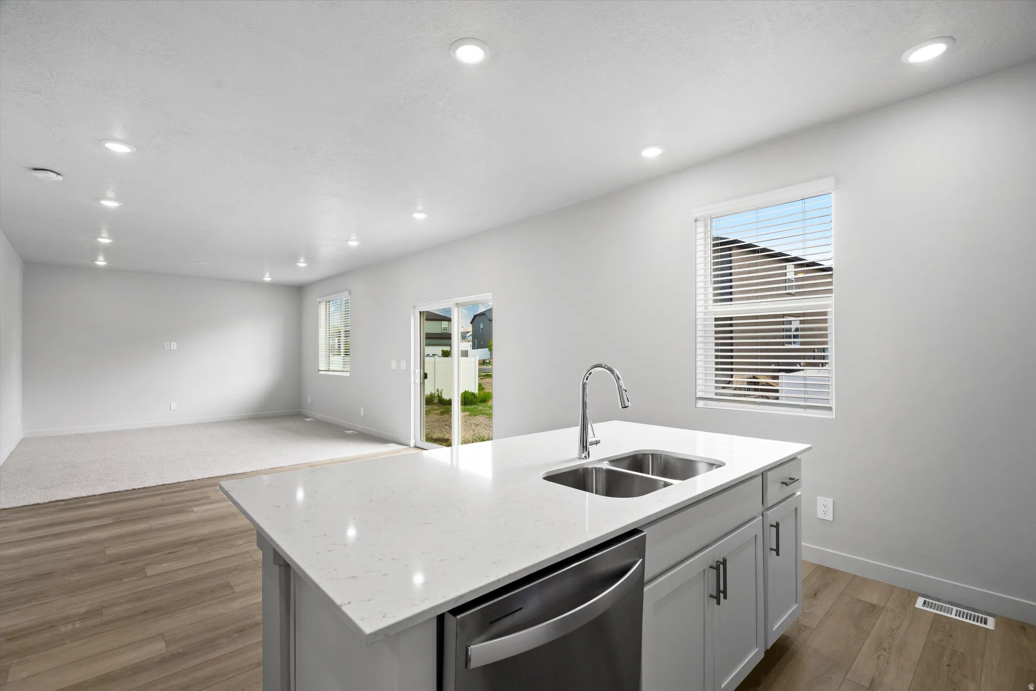 Kitchen with light wood-style flooring, light stone countertops, dishwasher, an island with sink, and open floor plan
