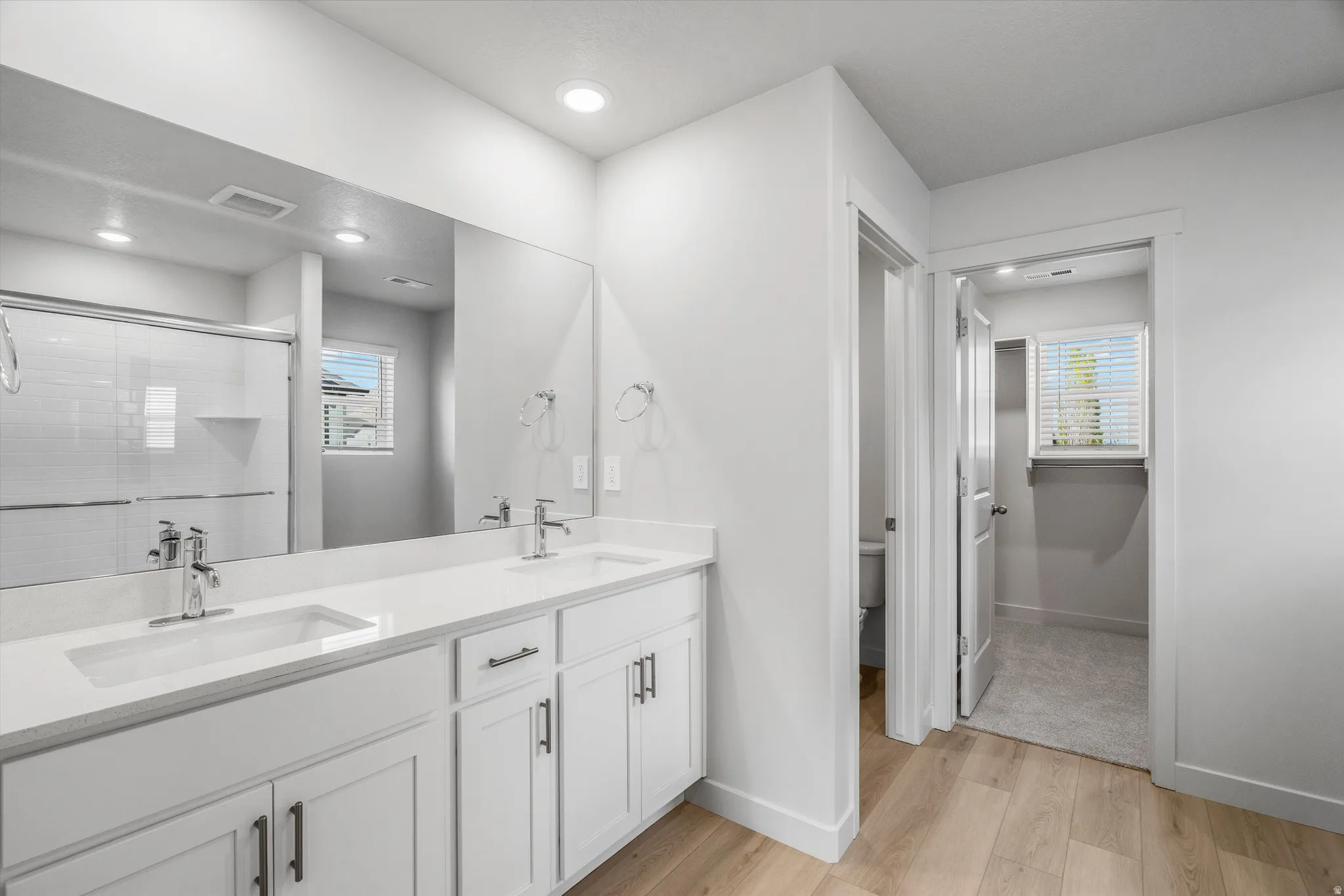 Full bathroom with double vanity, light wood-type flooring, a shower stall, plenty of natural light, and recessed lighting