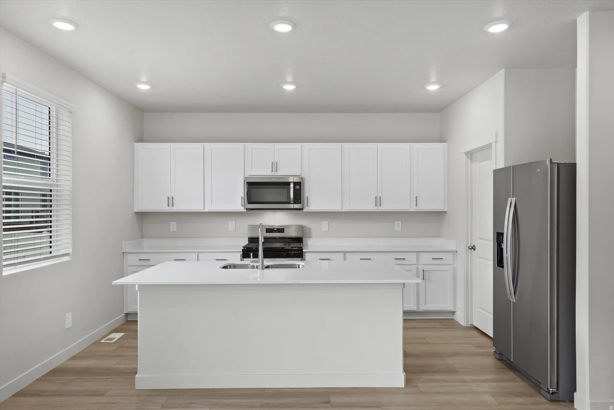 Kitchen featuring stainless steel appliances, white cabinets, light wood-style floors, a center island with sink, and recessed lighting