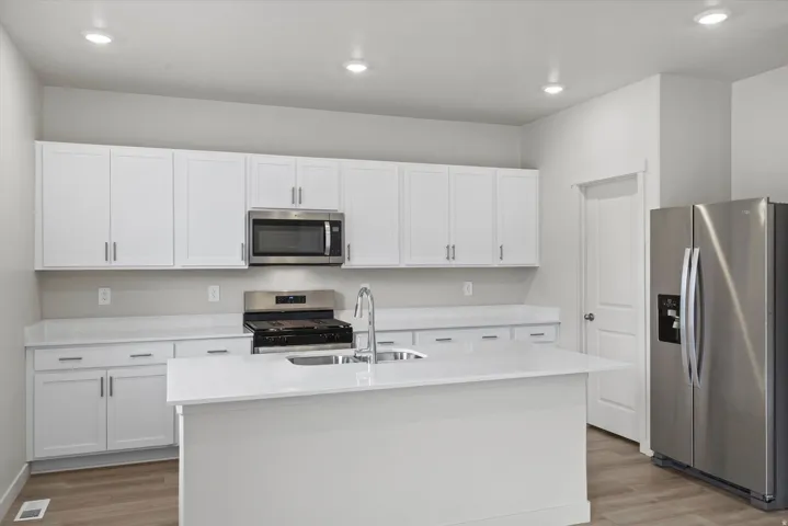 Kitchen with stainless steel appliances, white cabinets, a center island with sink, light stone countertops, and light wood-style floors