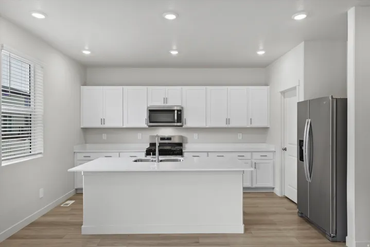 Kitchen featuring stainless steel appliances, white cabinets, light wood-style floors, a center island with sink, and recessed lighting