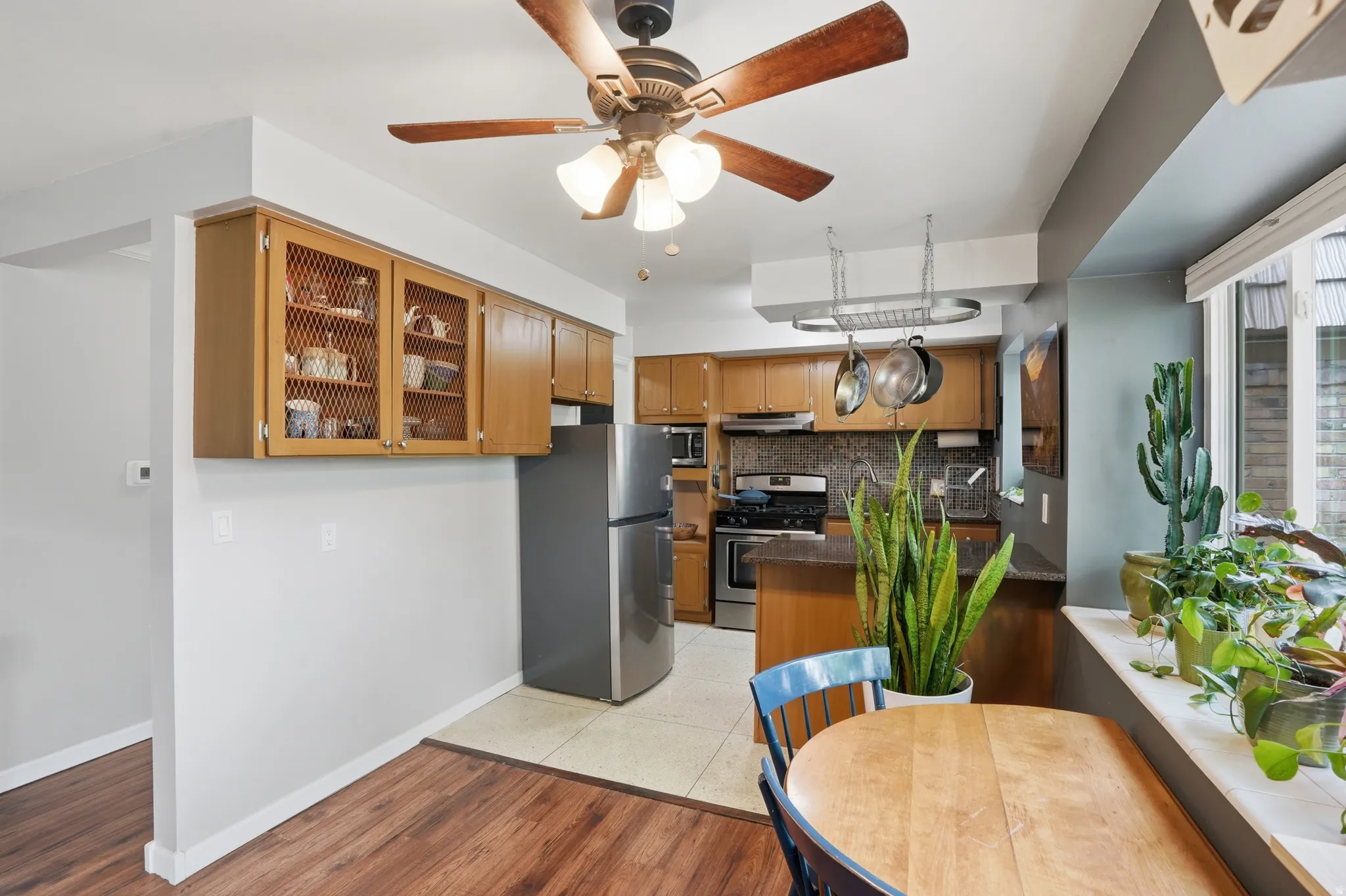 Kitchen featuring glass fronted cabinets, stainless steel appliances, backsplash, ceiling fan, and light wood-style flooring