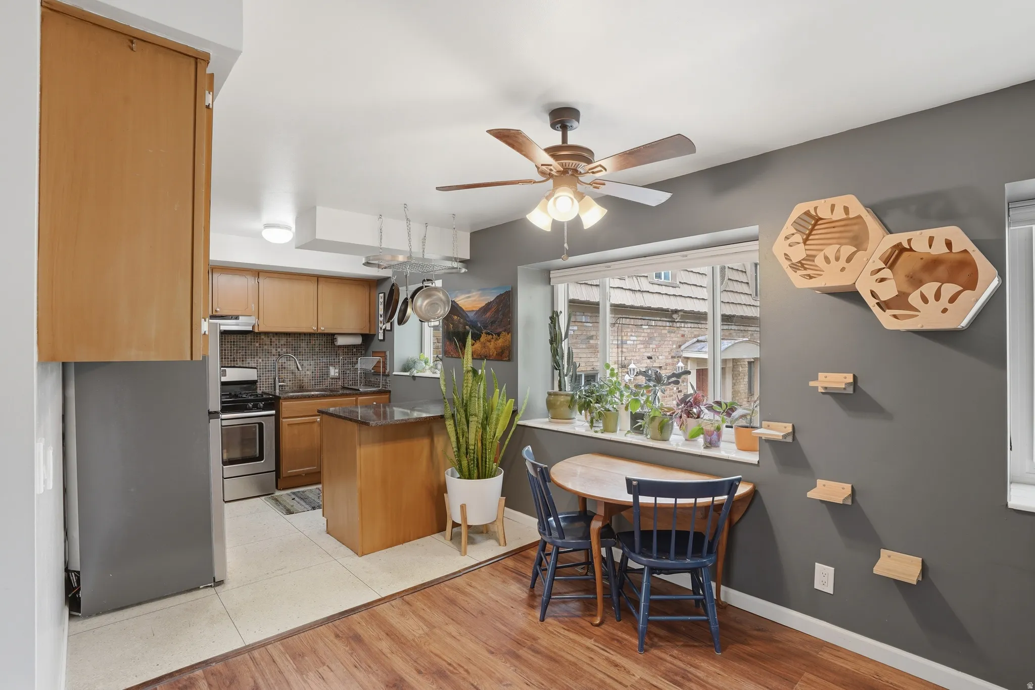 Kitchen featuring stainless steel appliances, light wood-style floors, a ceiling fan, dark stone counters, and decorative backsplash