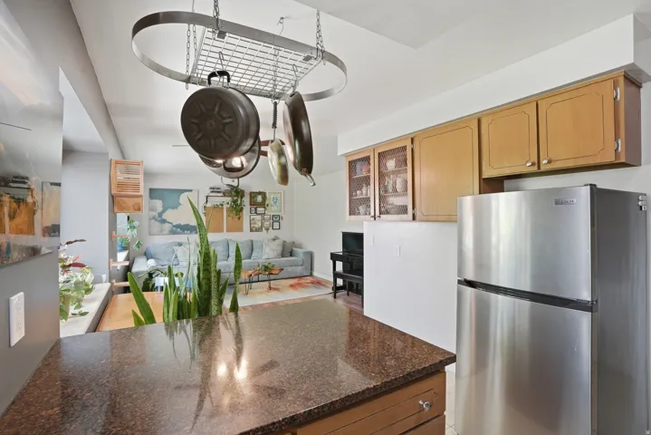 Kitchen featuring freestanding refrigerator, glass insert cabinets, dark stone counters, open floor plan, and a peninsula