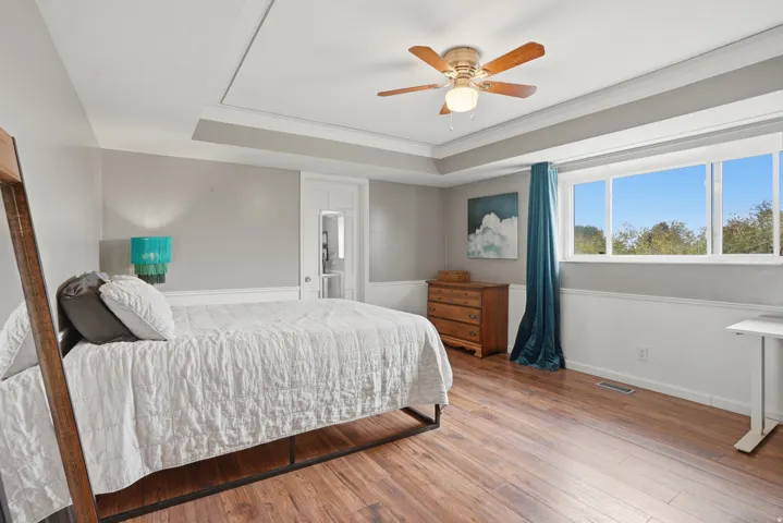 Bedroom with wood-type flooring, a ceiling fan, ornamental molding, and a raised ceiling