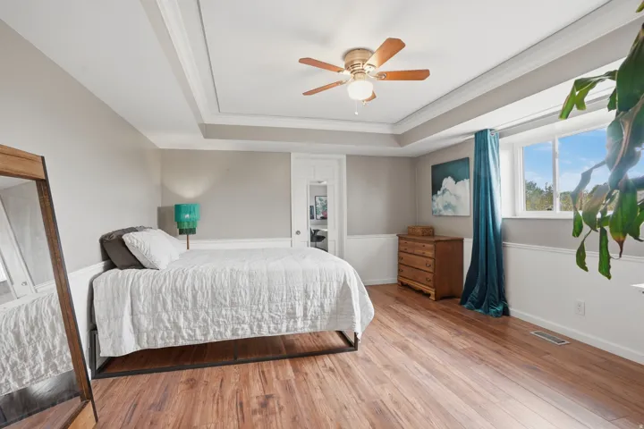 Bedroom with crown molding, wood finished floors, a ceiling fan, and a raised ceiling