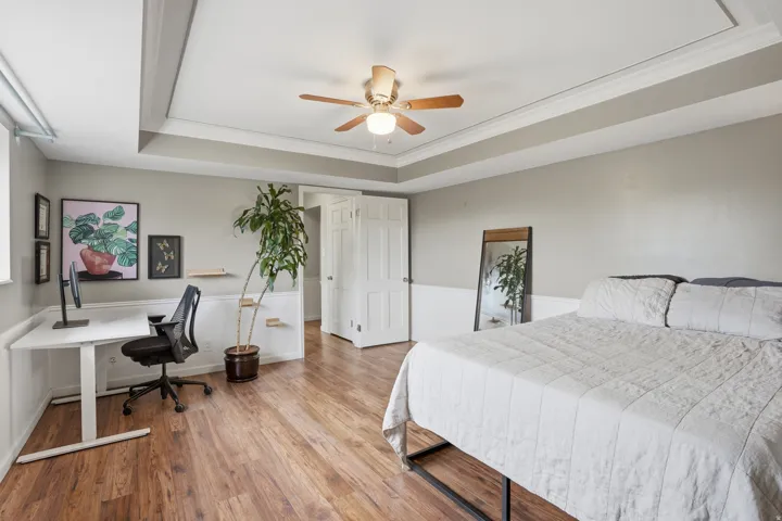 Bedroom with light wood-type flooring, an office area, crown molding, a ceiling fan, and a tray ceiling