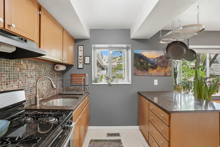 Kitchen featuring stainless steel gas range, a peninsula, dark stone counters, backsplash, and wood finish cabinets