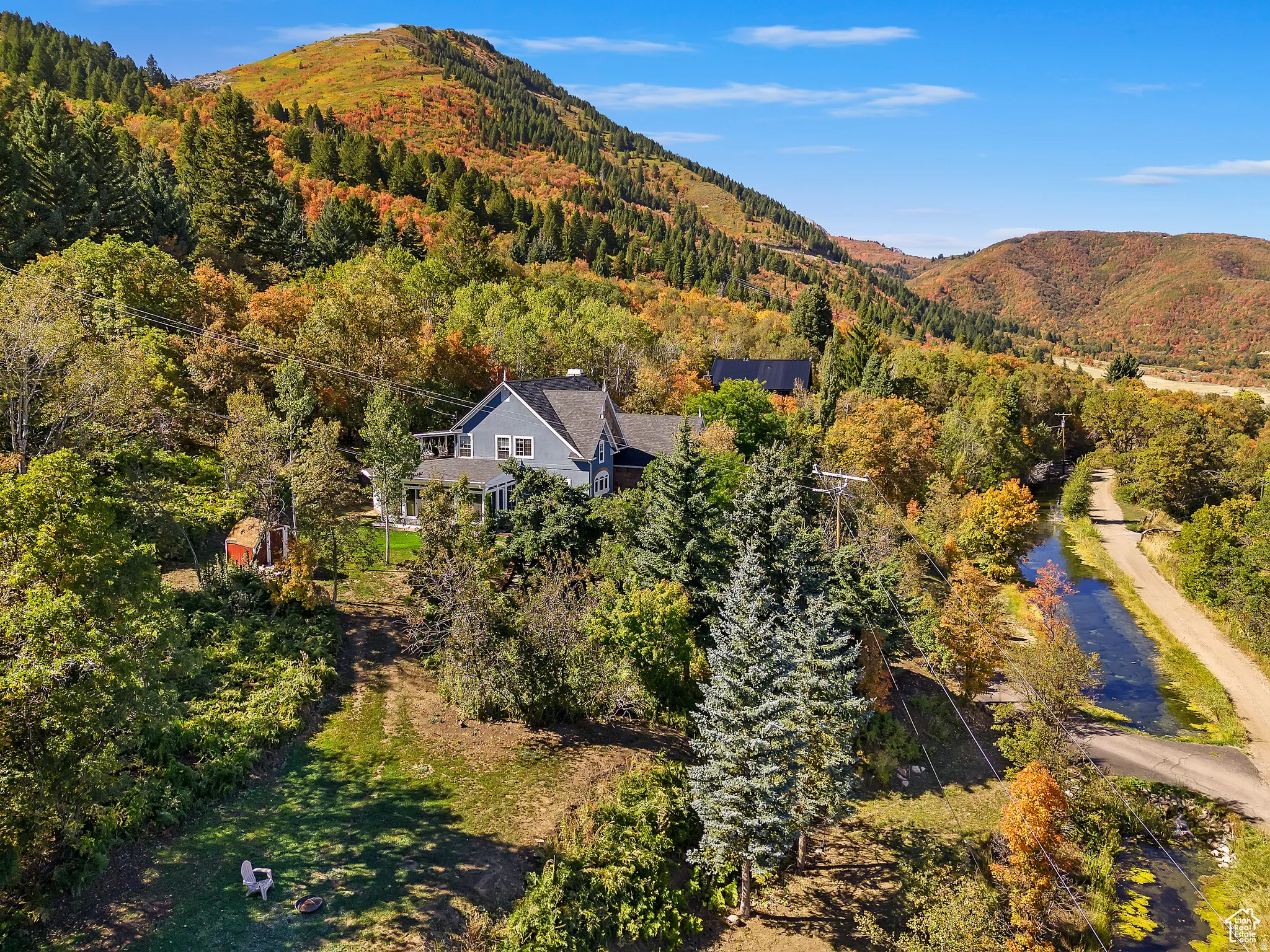 Expansive property featuring a grey residence with a dark roof and white trim, surrounded by mature trees in various autumnal colors