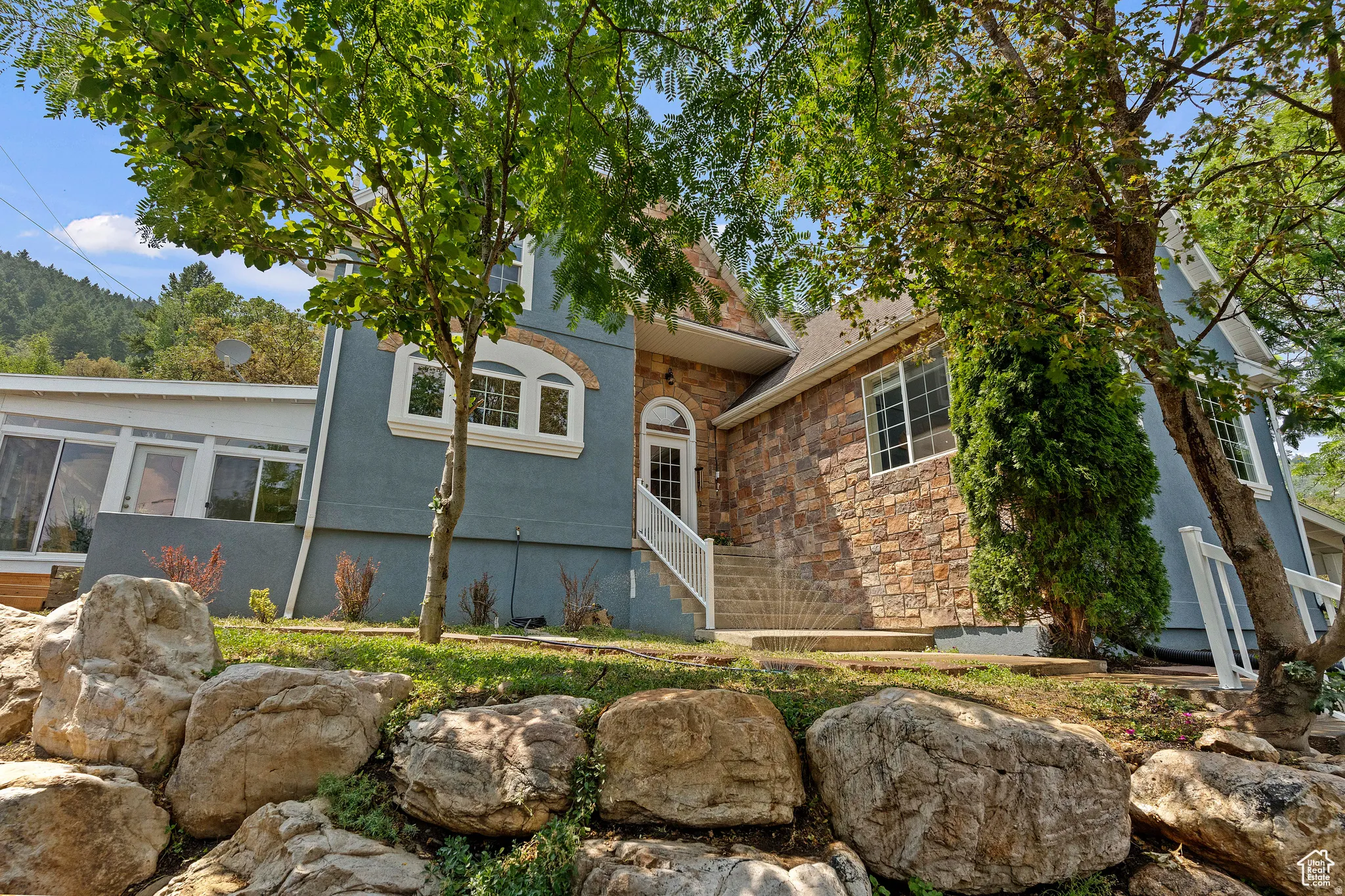 Stone and stucco exterior with multiple architectural windows, a prominent arched entry, white railing, and a tiered rock garden