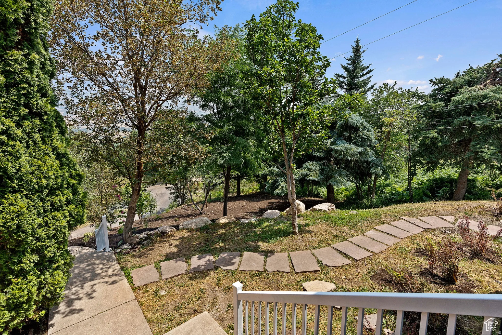 Terraced landscaping featuring a winding stone-paver pathway, mature trees, and natural rock accents