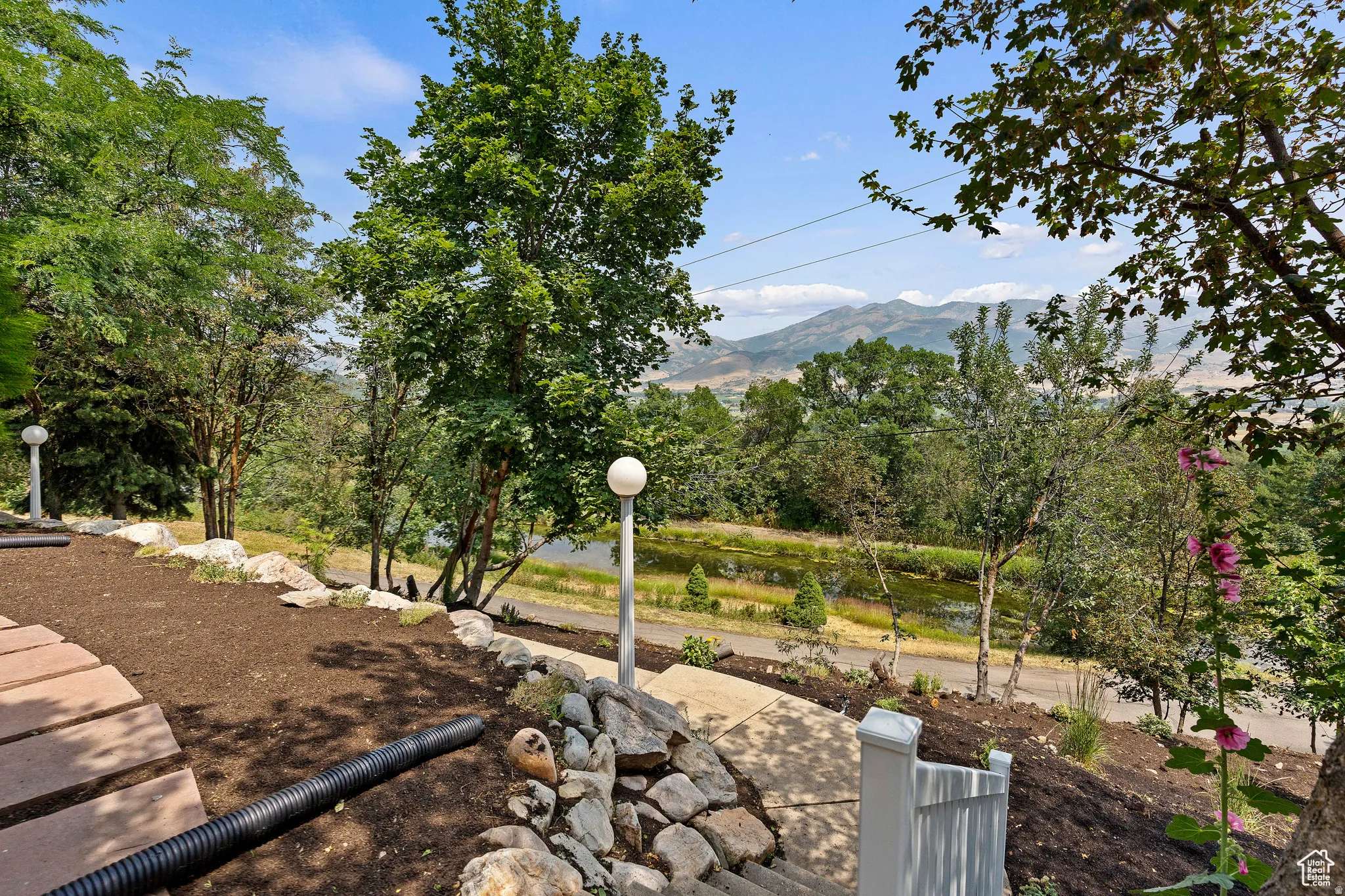 Terraced landscaping featuring mature trees, pathway lighting, and a stone-edged garden bed
