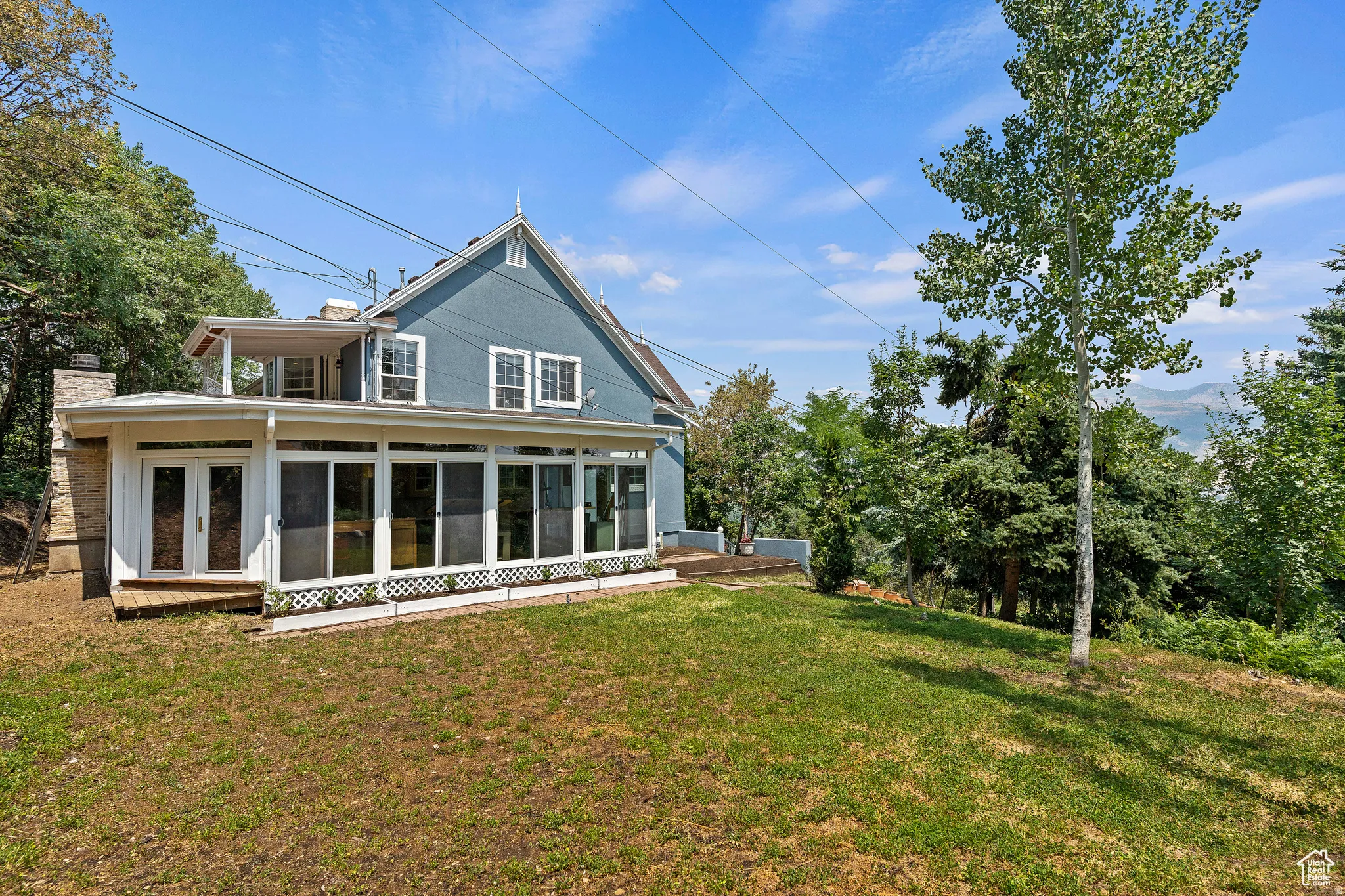 Expansive rear yard with a sloped lawn and mature trees