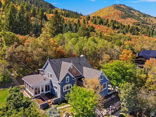 Blue exterior property featuring a sunroom, multiple rooflines, and dormer windows, complemented by surrounding mature trees and a distant mountain landscape