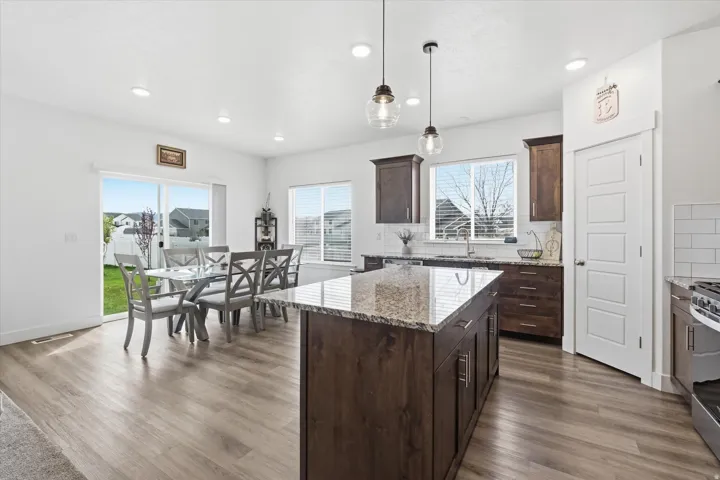 Kitchen with dark wood finish cabinetry, light stone counters, a kitchen island, backsplash, and dark wood finished floors