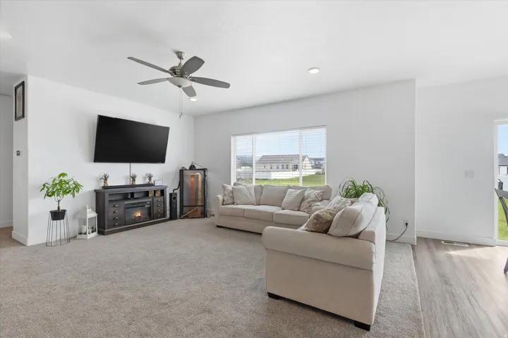 Living room with a ceiling fan, a warm lit fireplace, and recessed lighting