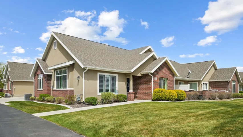 View of front of home featuring brick siding, a front yard, a shingled roof, and stucco siding