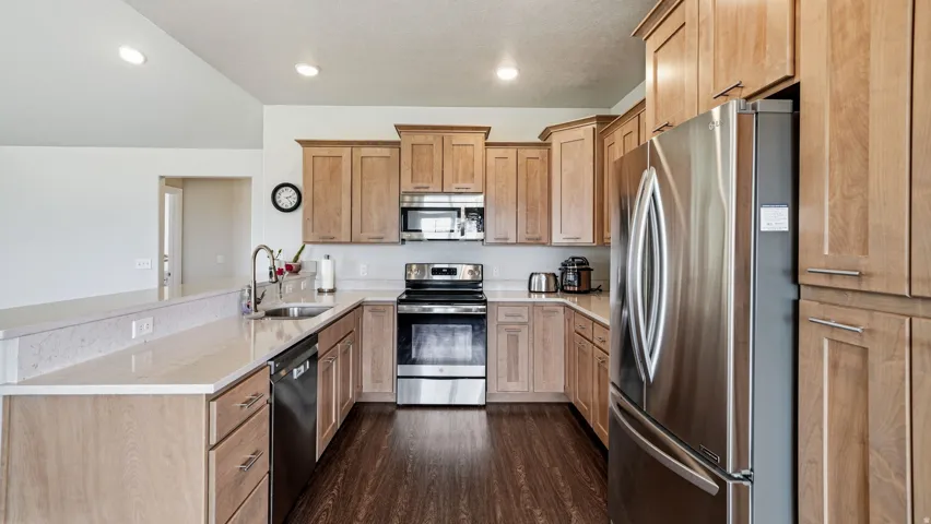 Kitchen with stainless steel appliances, a peninsula, light stone countertops, dark wood-type flooring, and recessed lighting