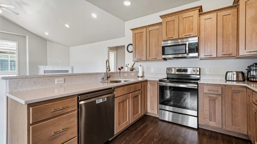 Kitchen featuring stainless steel appliances, a peninsula, light stone counters, vaulted ceiling, and dark wood finished floors