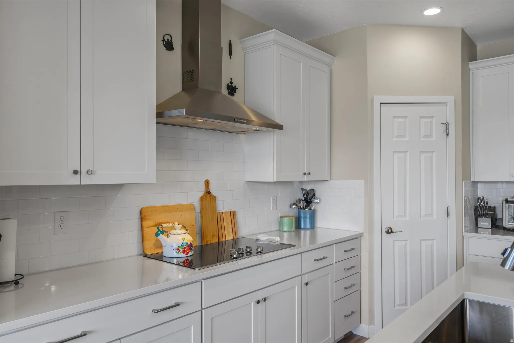 Kitchen with white cabinetry, black electric stovetop, decorative backsplash, and light stone counters