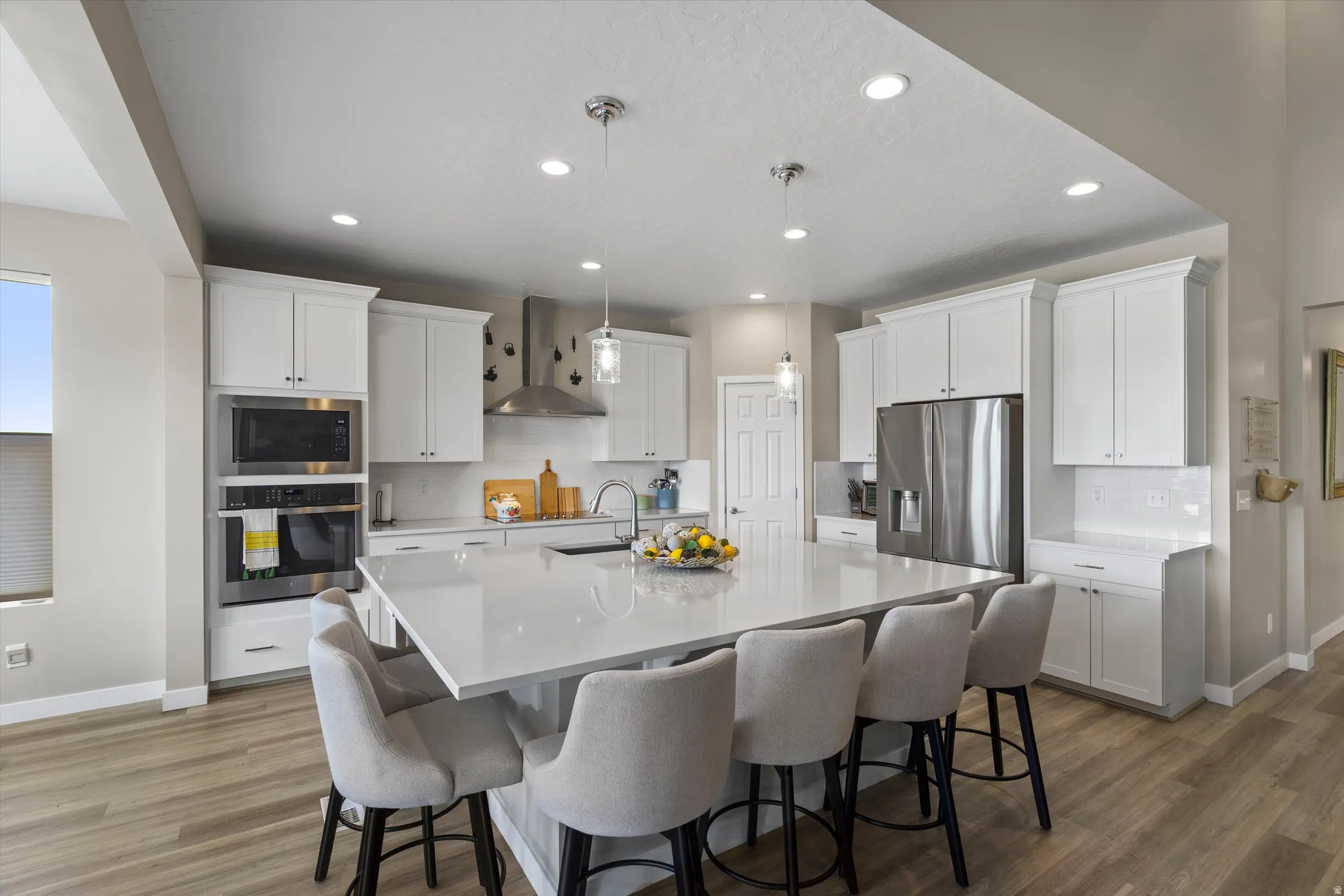 Kitchen with stainless steel appliances, white cabinets, a center island with sink, decorative light fixtures, and dark wood-type flooring