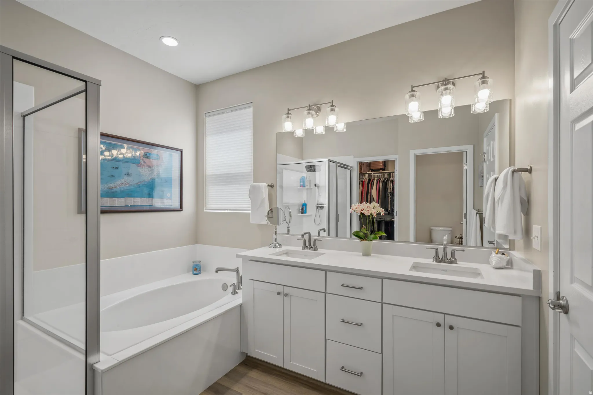 Bathroom with double vanity, a shower stall, a spacious closet, a garden tub, and light wood-style flooring