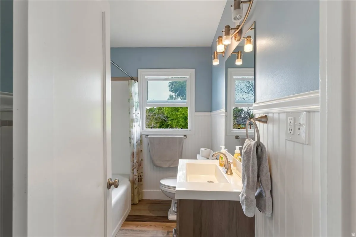 Bathroom featuring vanity, a wainscoted wall, light wood finished floors, and shower / bath combo