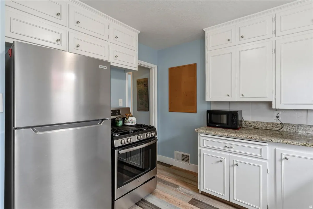 Kitchen with stainless steel appliances, white cabinets, and light wood-style flooring