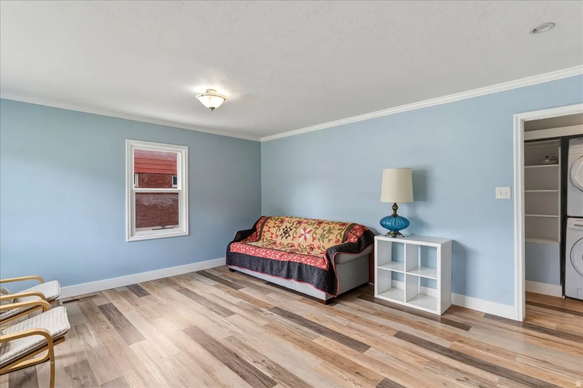 Living area with stacked washer and clothes dryer, crown molding, and light wood finished floors