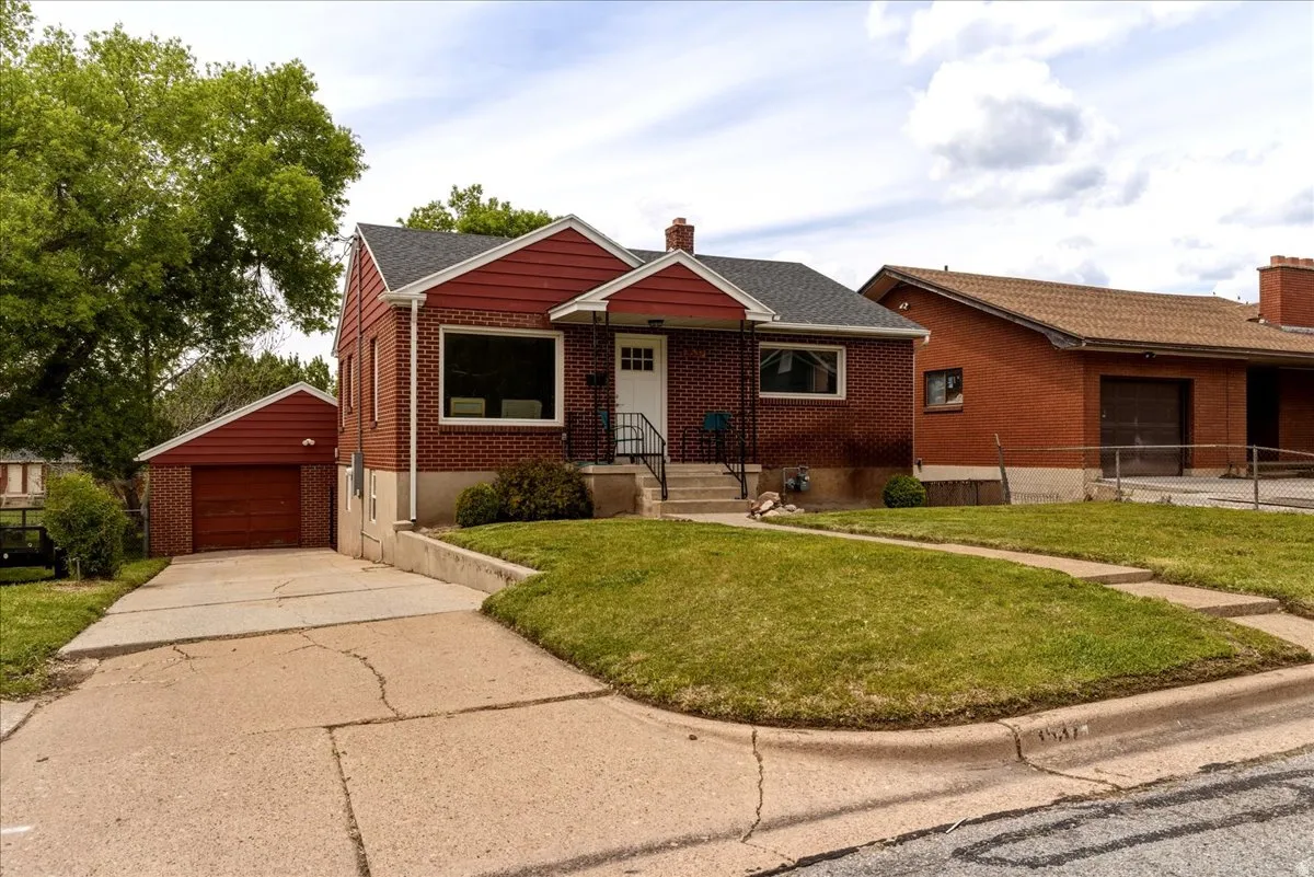 View of front of house with a chimney, a front lawn, an outdoor structure, brick siding, and a garage