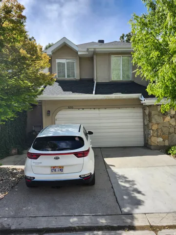 Traditional-style home featuring stucco siding, roof with shingles, driveway, stone siding, and an attached garage