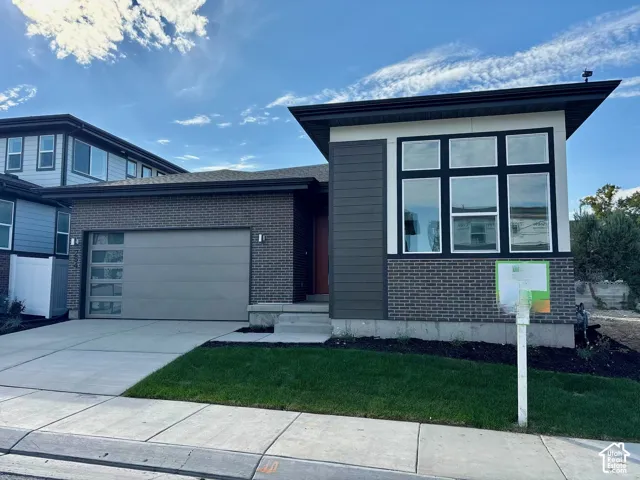Contemporary exterior featuring a modern garage door with glass panels, dark brick accents, and a contrasting siding facade