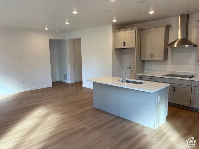 Open-concept living space featuring wood-finish flooring, recessed lighting, a kitchen island with an undermount sink, light-toned cabinetry, and a stainless steel range hood
