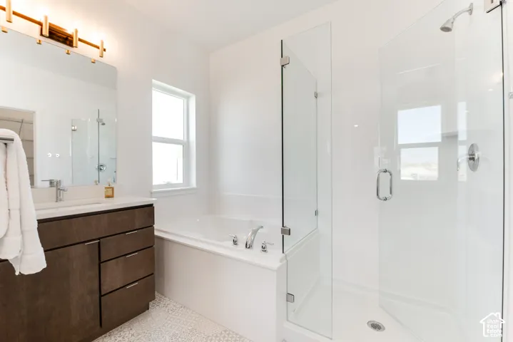 Glass-enclosed shower, built-in soaking tub, single vanity with integrated sink, white countertop, and patterned floor tile