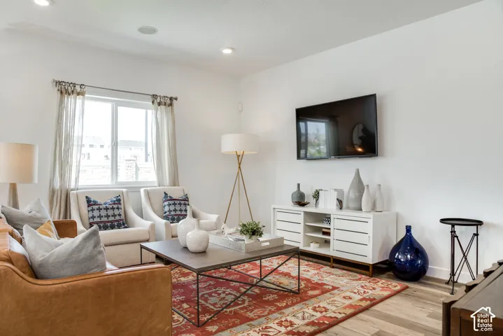 Recessed ceiling lighting, large window, wood-finish flooring, white walls, and a built-in media console