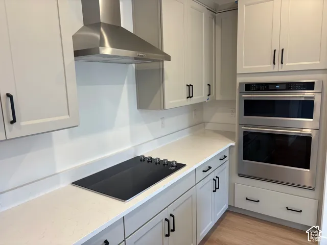 Integrated stainless steel double oven, stainless steel range hood, built-in cooktop, light-toned cabinetry, and wood-finish flooring