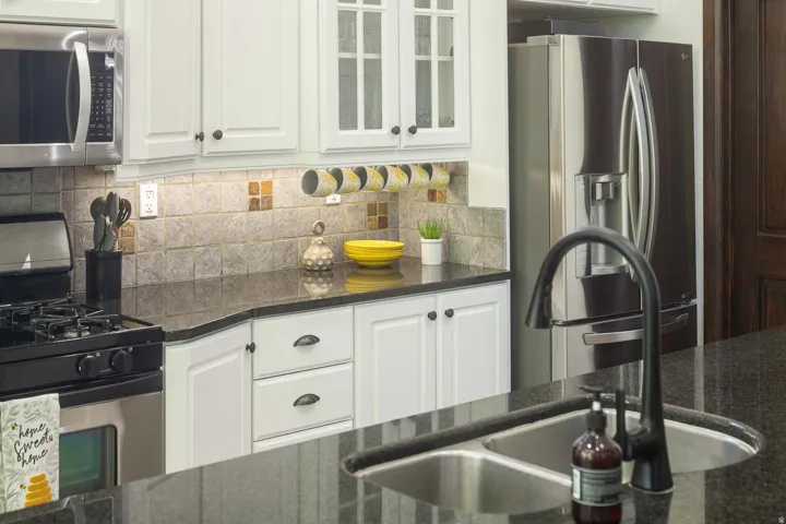 Kitchen featuring white cabinets, glass fronted cabinets, stainless steel appliances, dark stone countertops, and decorative backsplash