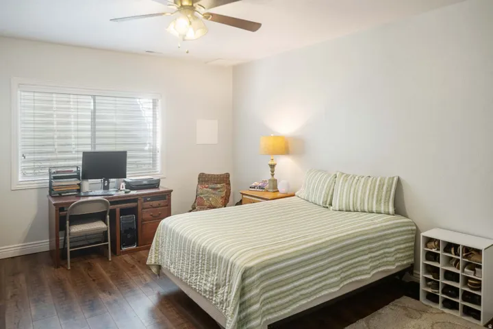 Bedroom with dark wood-style flooring, a ceiling fan, and an office area
