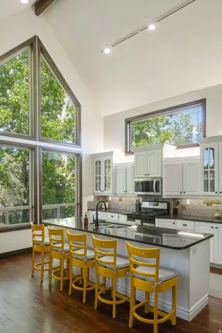 Kitchen featuring glass insert cabinets, stainless steel appliances, dark wood-style flooring, white cabinets, and a kitchen bar