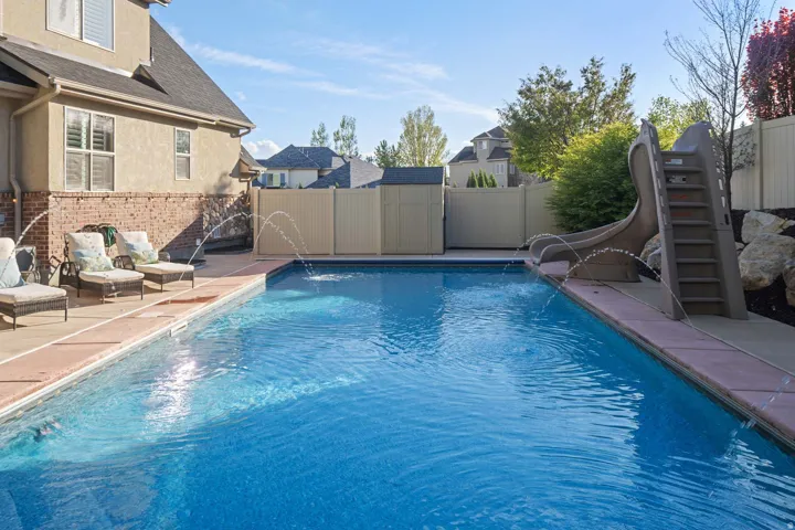 View of pool featuring a water slide, a fenced backyard, and patio surround
