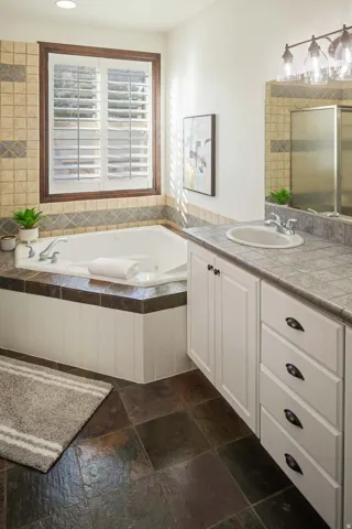 Bathroom featuring vanity, stone tile floors, a garden tub, and a tile shower