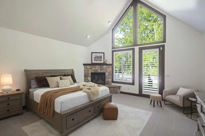 Bedroom with a high ceiling, light colored carpet, access to exterior, and a stone fireplace