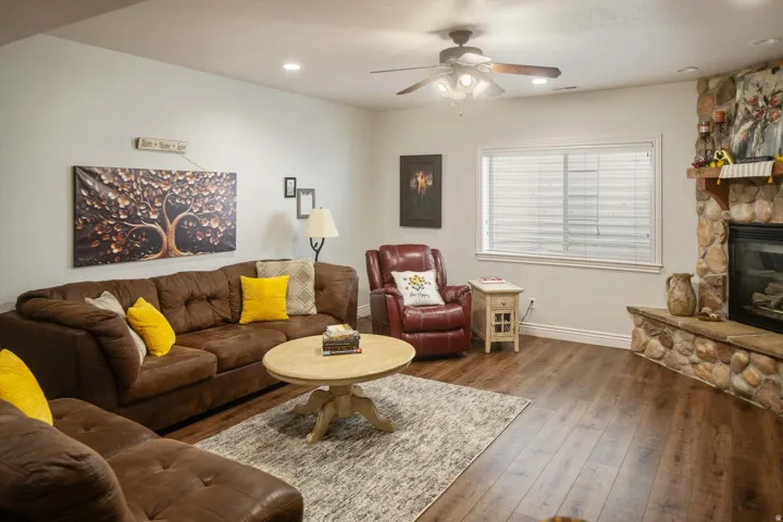 Living area with hardwood / wood-style floors, ceiling fan, a stone fireplace, and recessed lighting