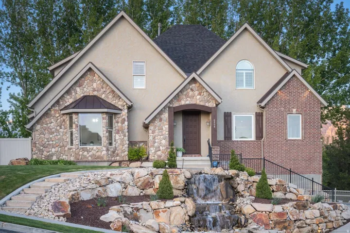 View of front of house featuring stucco siding, stone siding, a standing seam roof, and a small pond