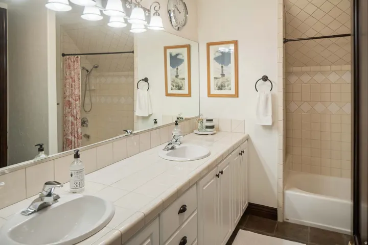 Full bath with double vanity, shower / bath combination with curtain, and dark tile patterned flooring