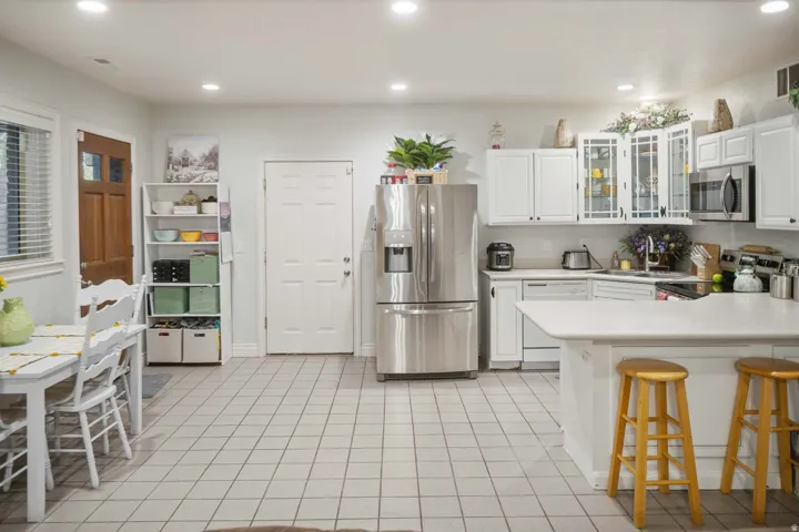 Kitchen with glass fronted cabinets, stainless steel appliances, light countertops, white cabinetry, and a breakfast bar