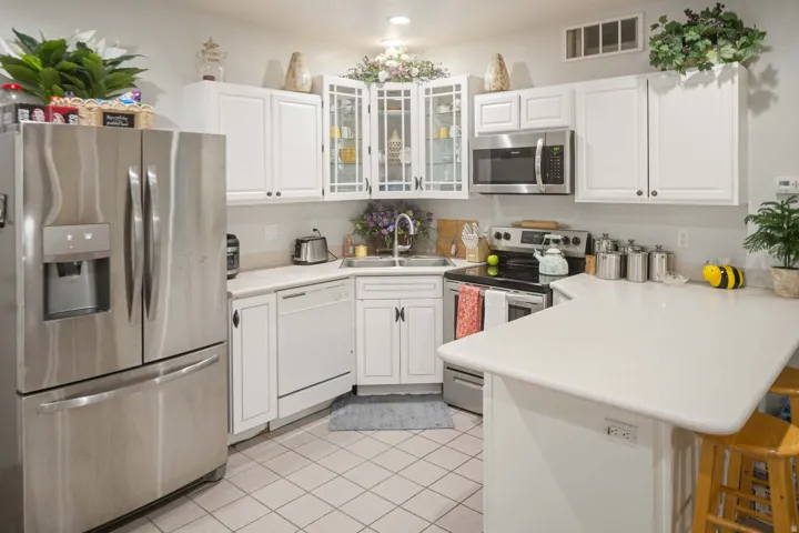 Kitchen featuring stainless steel appliances, white cabinets, light countertops, glass insert cabinets, and a peninsula
