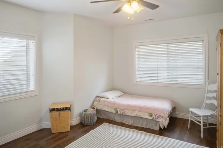 Bedroom with dark wood-style flooring, a ceiling fan, and multiple windows